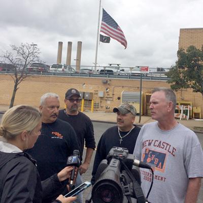 Local 100 members talk to media in front of lowered flag